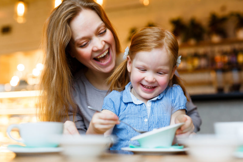 Cheerful woman and her little daughter eating in cafe