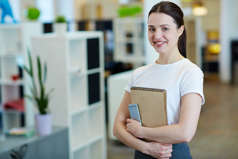 Young woman smiling happily while looking at camera standing in modern office