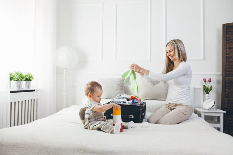 Travelling with kids. Happy mother with her child packing clothes for their holiday