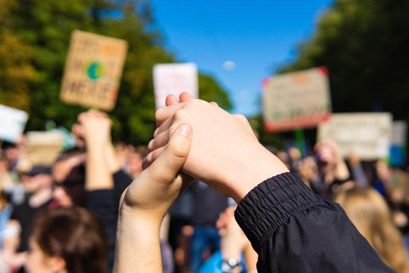 two young people at a rally, joining hands together signaling peace, unity and decisiveness in front of a crowd carrying protest placards