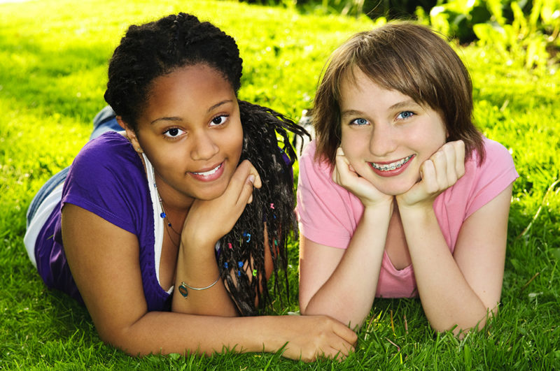 Two happy teenage girls laying on grass