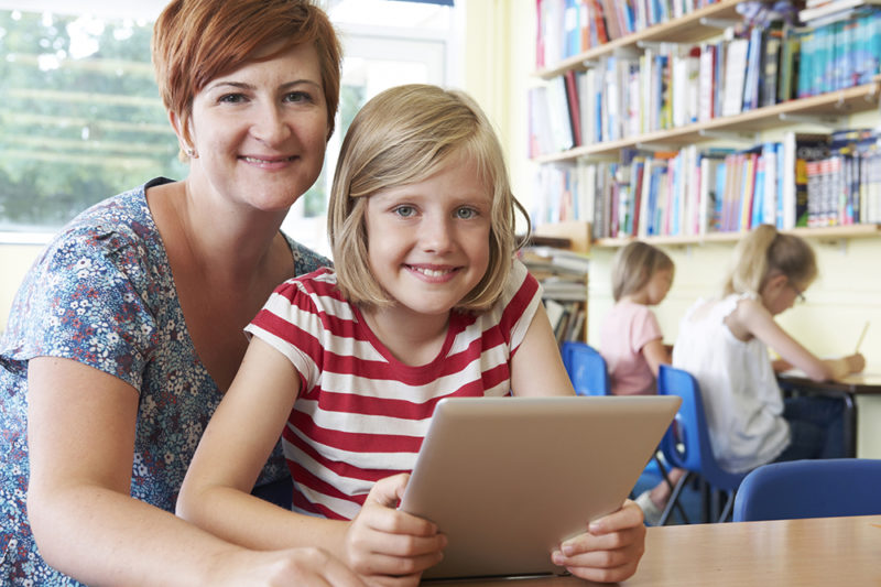 Young girl With Teacher Using Digital Tablet Computer In Class