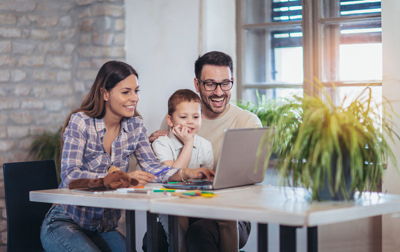 A modern family using a laptop, mom, dad and their five year old son