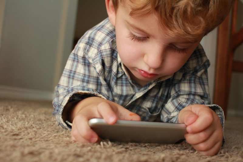 boy holding smartphone while lying on rug