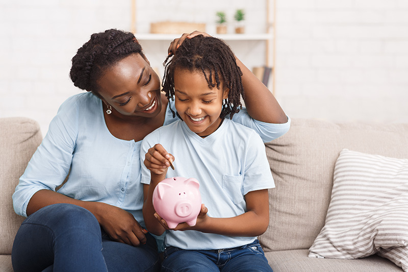 African American mother and daughter putting money in piggy bank