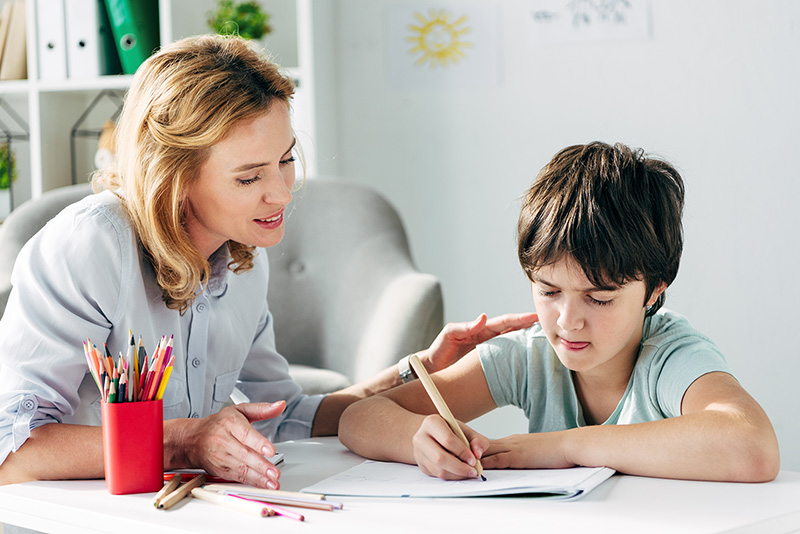 child drawing with pencil and child psychologist looking on