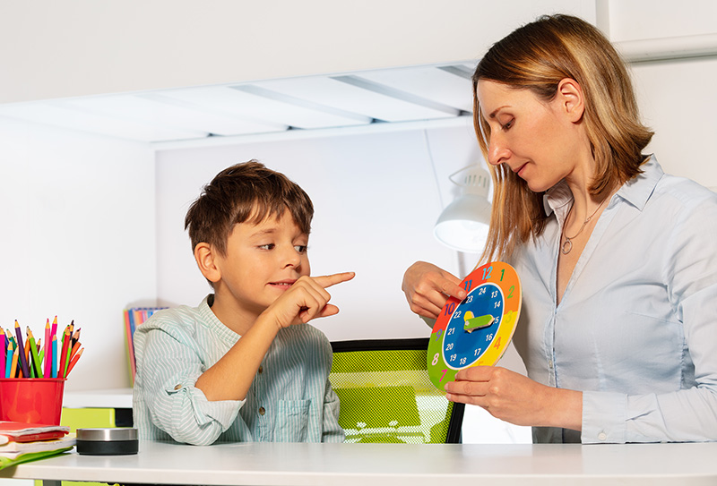 Child with autism spectrum disorder learns clock and hours, teacher during ABA therapy class