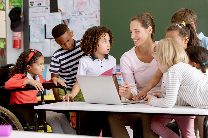 Teacher and students discussing over laptop in classroom