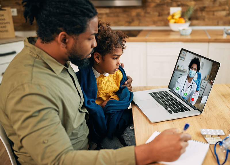 Black father and daughter communicating with a doctor via video call from home during COVID-19 pandemic