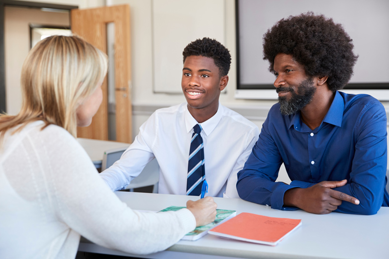 Father and son speaking with teacher at school