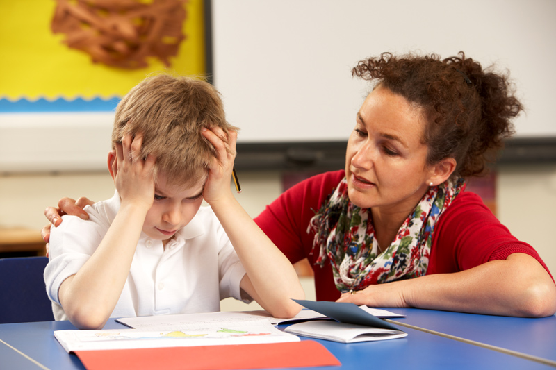 Stressed boy at school working In classroom with teacher