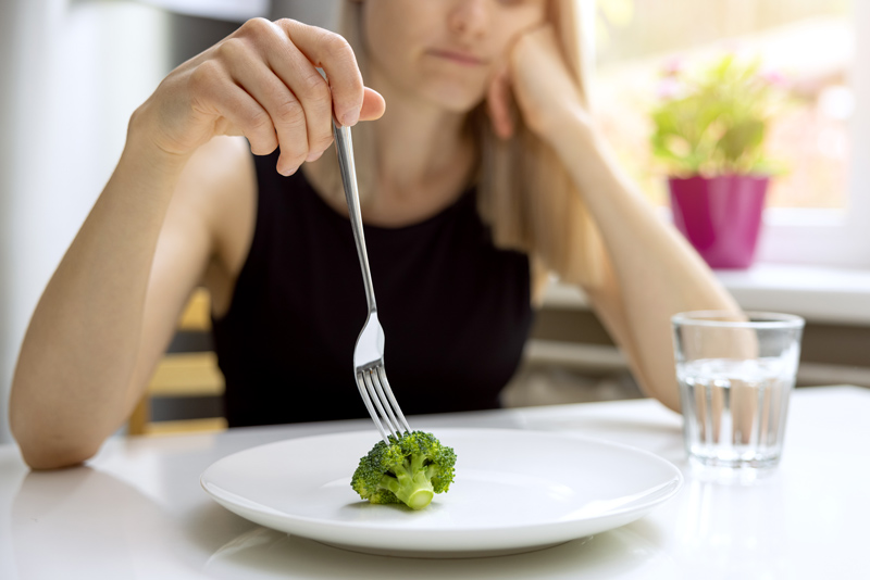 dieting problems, eating disorder - unhappy woman looking at small broccoli portion on the plate