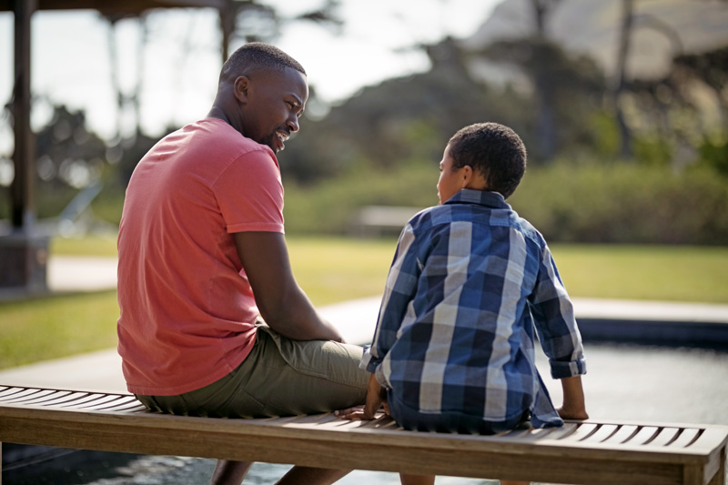 African American father talking with his son on a bench outside