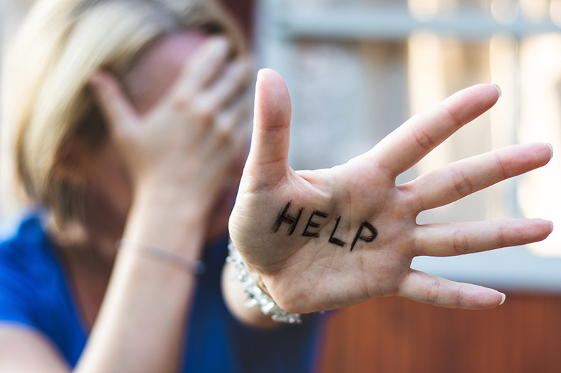 Woman suffering with depression gesturing with a help sign on her hand