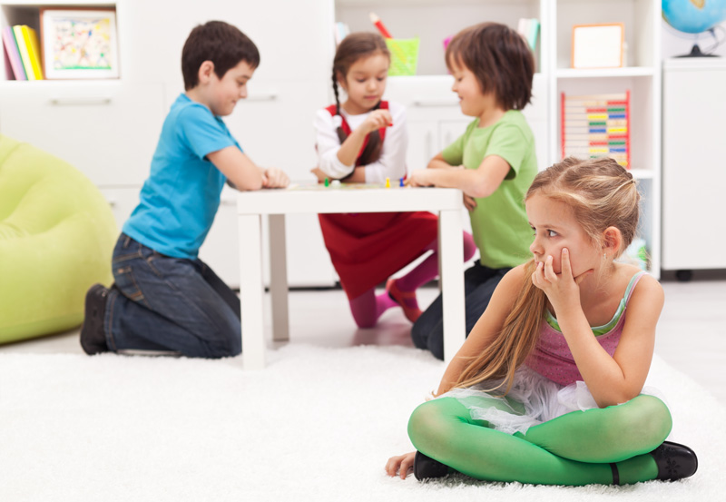 Little girl sitting apart - feeling excluded by the others with no friends