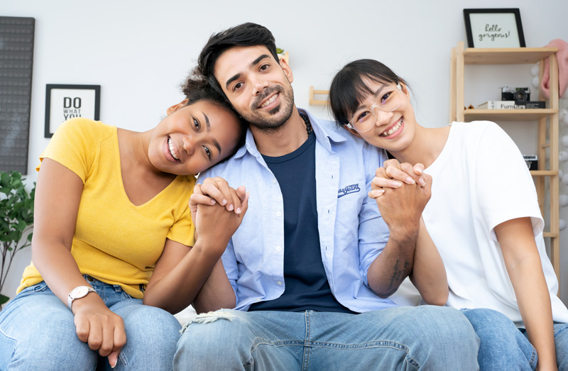 Man sitting with two women holding hands in a non-monogamous relationship