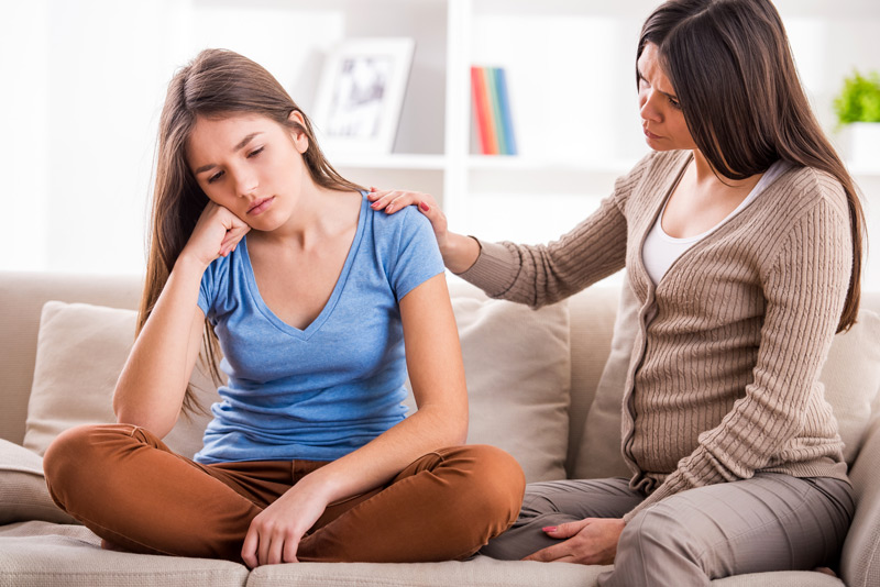 Mother comforting her teen daughter on a couch at home